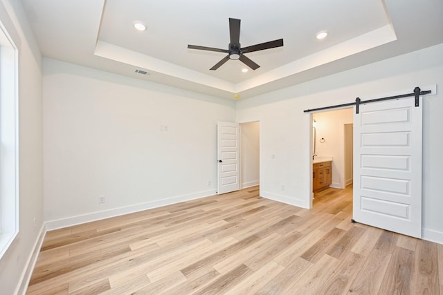 unfurnished bedroom featuring light wood-style flooring, visible vents, baseboards, a barn door, and a raised ceiling