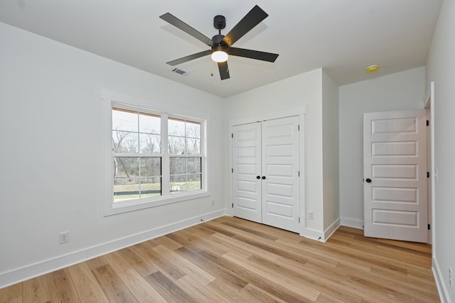 unfurnished bedroom featuring a closet, light wood-style floors, baseboards, and ceiling fan