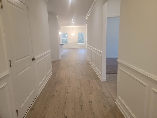 corridor with light wood-style floors, a decorative wall, crown molding, and a wainscoted wall