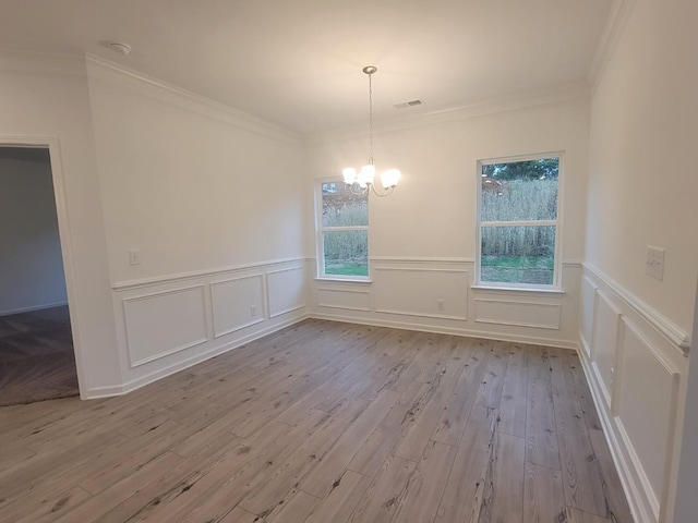 unfurnished dining area featuring wood finished floors, ornamental molding, visible vents, wainscoting, and a notable chandelier