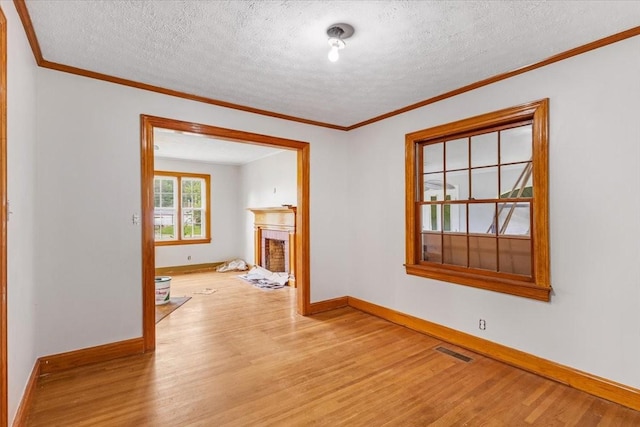 unfurnished living room with wood finished floors, visible vents, a fireplace, crown molding, and baseboards
