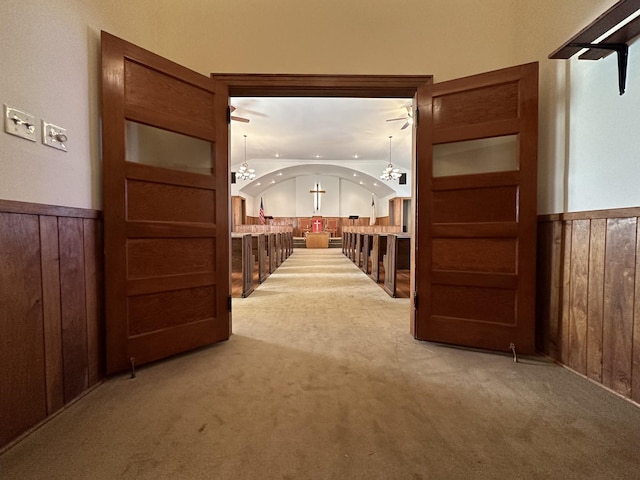 corridor with carpet flooring, wood walls, a chandelier, and wainscoting