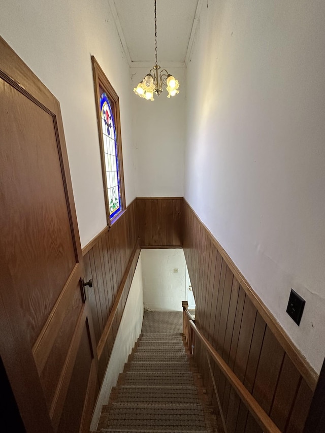 stairway featuring an inviting chandelier, wood walls, wainscoting, and crown molding