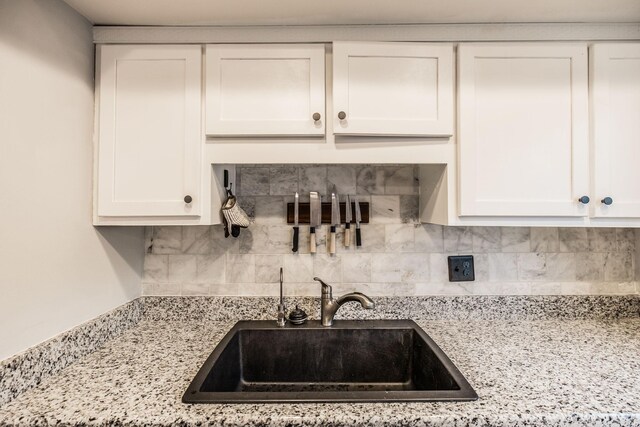 kitchen with a sink, white cabinets, decorative backsplash, and light stone countertops