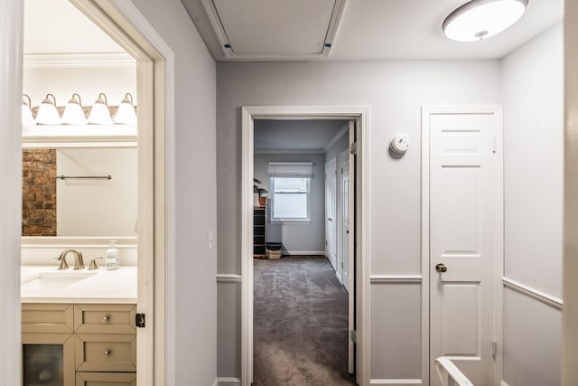hall with a sink and dark colored carpet