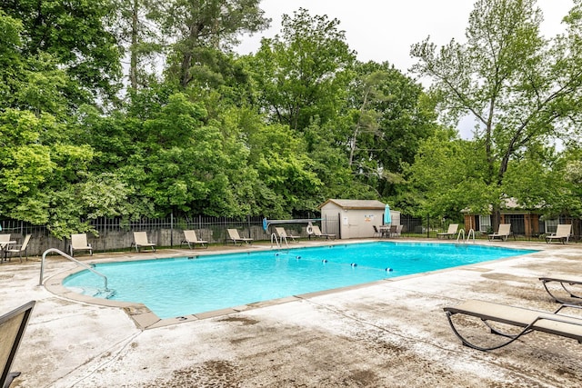 community pool featuring a patio, fence, view of wooded area, and a shed