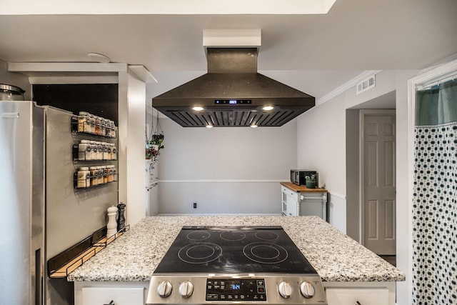kitchen with island range hood, stainless steel range with electric stovetop, light stone countertops, and freestanding refrigerator