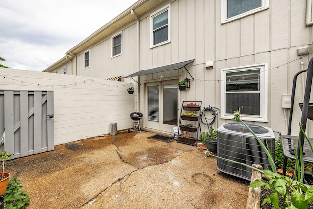 rear view of house with cooling unit, fence, a patio, and board and batten siding
