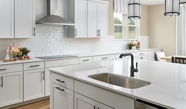 kitchen featuring a sink, wall chimney range hood, black electric cooktop, and white cabinets