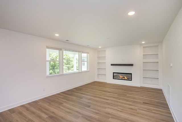 138 W Cassa Way, Mount Juliet, TN 37122 - unfurnished living room featuring baseboards, light wood-type flooring, built in shelves, recessed lighting, and a glass covered fireplace