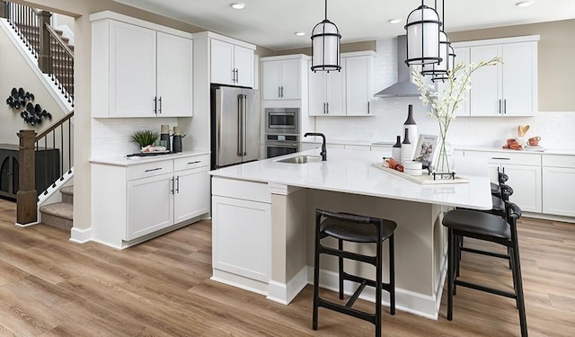 kitchen with wall chimney range hood, appliances with stainless steel finishes, tasteful backsplash, and a sink