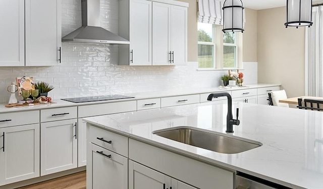 kitchen featuring light stone countertops, a sink, wall chimney exhaust hood, black electric cooktop, and white cabinets