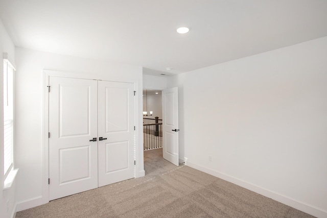 unfurnished bedroom with light colored carpet, a closet, baseboards, and recessed lighting