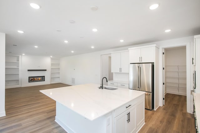 kitchen featuring a sink, high end refrigerator, light wood-style floors, light stone counters, and built in shelves