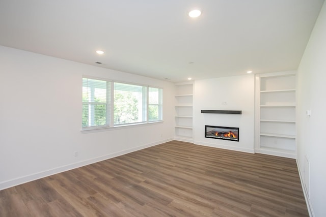 unfurnished living room featuring wood finished floors, built in shelves, recessed lighting, baseboards, and a glass covered fireplace