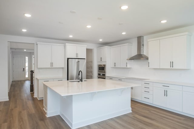 kitchen featuring a sink, wall chimney exhaust hood, backsplash, stainless steel appliances, and a kitchen island with sink