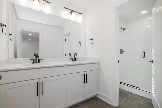 full bathroom featuring double vanity, baseboards, a stall shower, and a sink