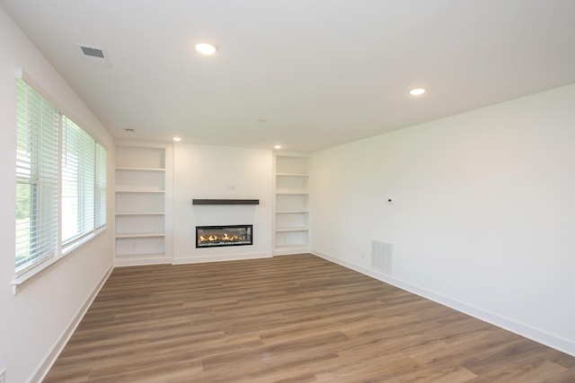 unfurnished living room featuring wood finished floors, visible vents, built in features, recessed lighting, and baseboards