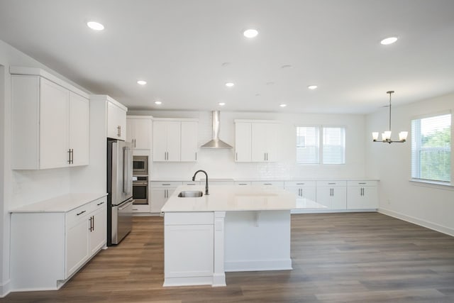 kitchen featuring a sink, a chandelier, wall chimney range hood, a center island with sink, and stainless steel appliances