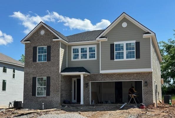 view of front of home featuring central AC, driveway, brick siding, and an attached garage