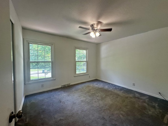 unfurnished room with a textured ceiling, baseboards, dark colored carpet, ceiling fan, and visible vents