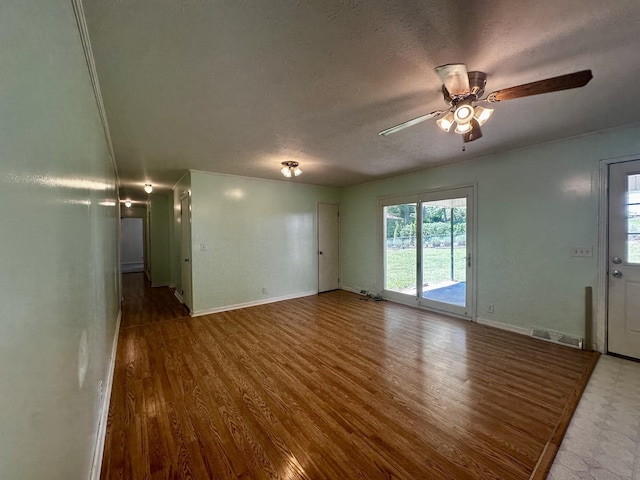 unfurnished living room featuring wood finished floors, a textured ceiling, visible vents, baseboards, and ceiling fan