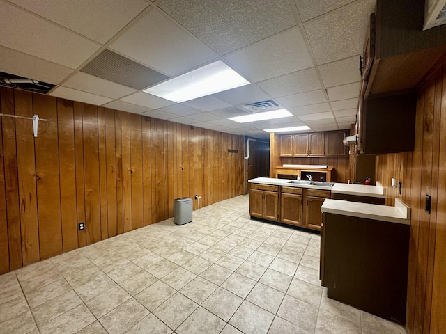 kitchen featuring a drop ceiling, a sink, brown cabinetry, light countertops, and wooden walls