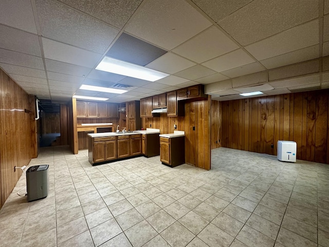 kitchen with open floor plan, a paneled ceiling, wood walls, light countertops, and a kitchen island