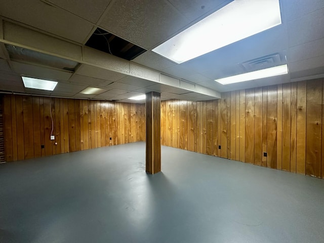 finished basement featuring a drop ceiling, wooden walls, and visible vents