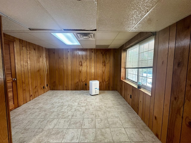 unfurnished room with a paneled ceiling, wooden walls, and visible vents