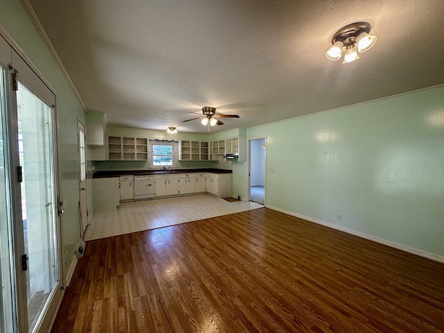 unfurnished living room featuring a sink, wood finished floors, ornamental molding, ceiling fan, and baseboards