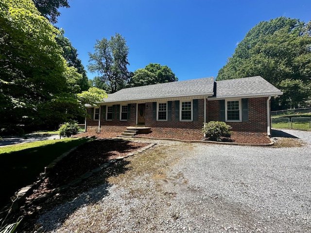 single story home featuring driveway, brick siding, a shingled roof, and fence