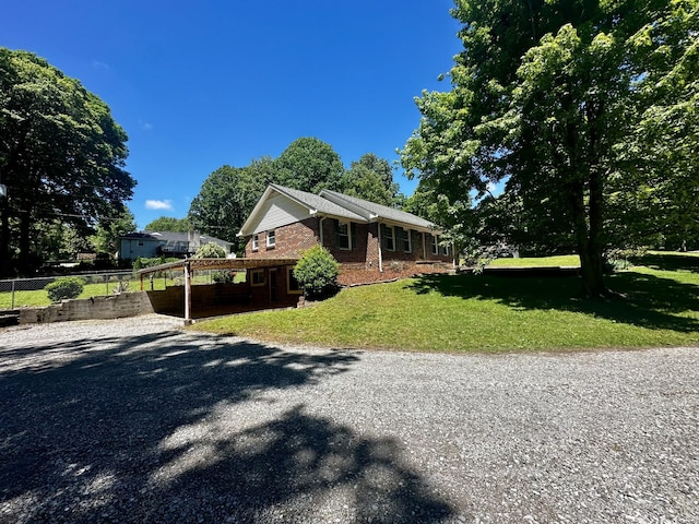view of front of home featuring gravel driveway, a front yard, brick siding, and fence