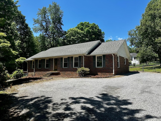ranch-style house featuring gravel driveway, brick siding, and fence