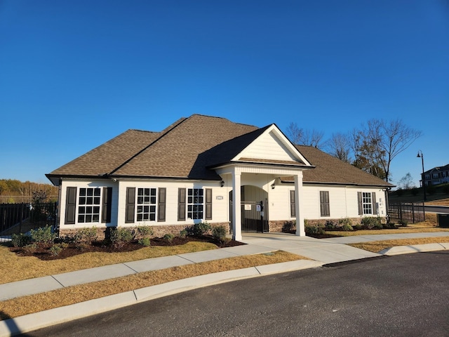 view of front facade featuring concrete driveway, stone siding, roof with shingles, and fence