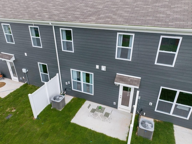 back of house with a yard, central air condition unit, roof with shingles, and fence