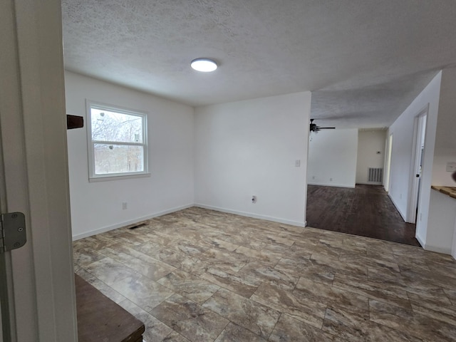 spare room with baseboards, ceiling fan, visible vents, and a textured ceiling
