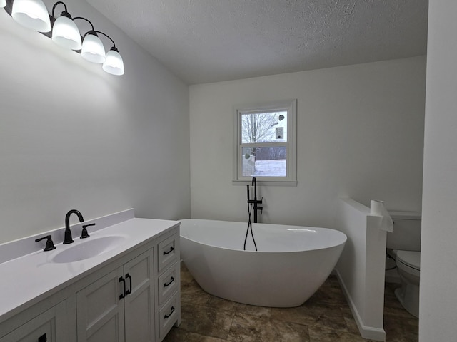 bathroom with a textured ceiling, toilet, baseboards, a soaking tub, and vanity