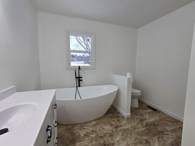 bathroom featuring toilet, baseboards, vanity, and a freestanding bath