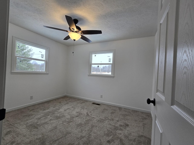 carpeted empty room with a textured ceiling, baseboards, a ceiling fan, and visible vents