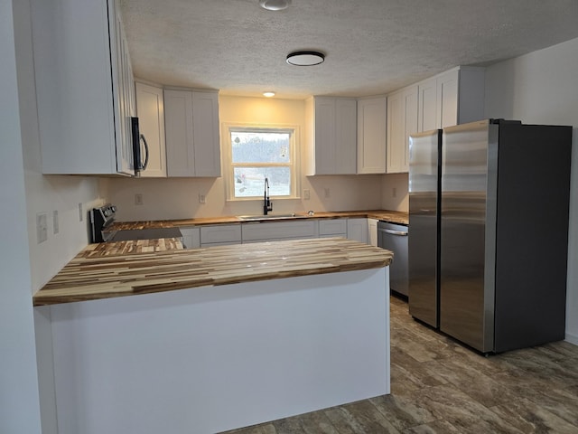 kitchen with butcher block countertops, a peninsula, stainless steel appliances, a sink, and a textured ceiling