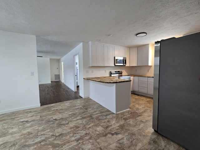 kitchen with wooden counters, visible vents, white cabinetry, open floor plan, and stainless steel appliances