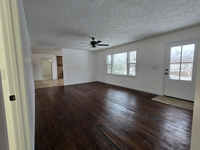 unfurnished living room with a ceiling fan, a textured ceiling, baseboards, dark wood-style flooring, and visible vents