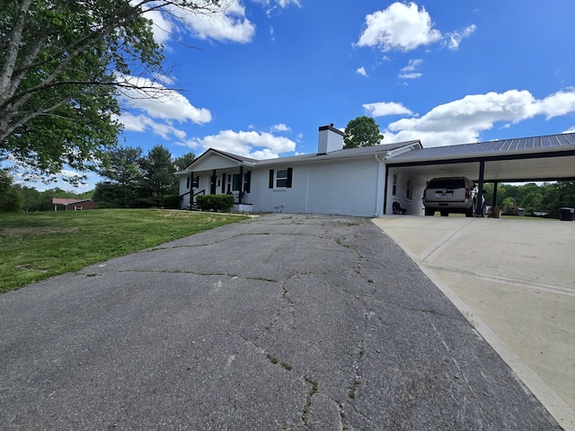 ranch-style home with concrete driveway, a front yard, a chimney, and an attached carport