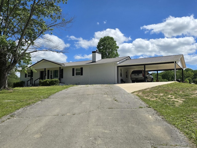 ranch-style home with driveway, a front yard, metal roof, an attached carport, and a chimney