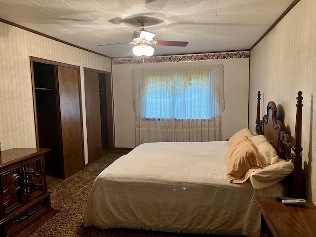 carpeted bedroom featuring a ceiling fan, crown molding, two closets, and wallpapered walls