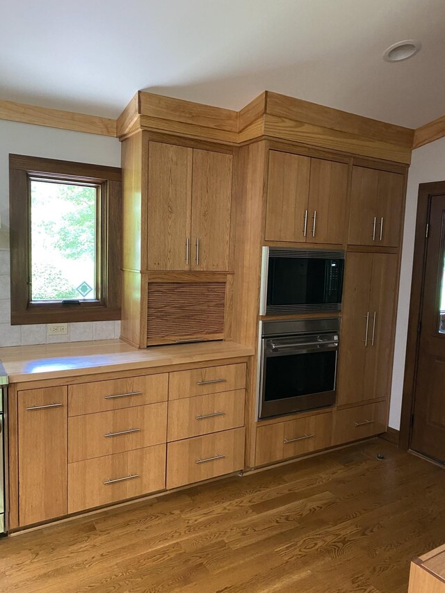 kitchen with black microwave, wall oven, light countertops, and light wood-type flooring
