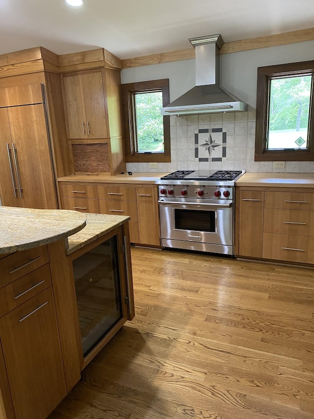 kitchen featuring light wood-style flooring, backsplash, designer stove, and wall chimney exhaust hood