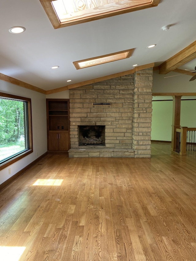 unfurnished living room featuring recessed lighting, baseboards, a stone fireplace, wood finished floors, and vaulted ceiling with skylight