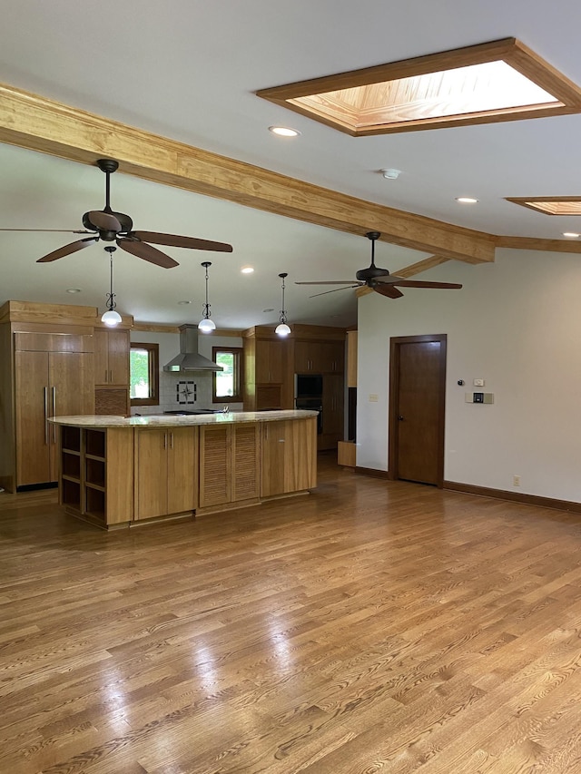 kitchen with wall chimney range hood, light wood-style floors, baseboards, and a ceiling fan